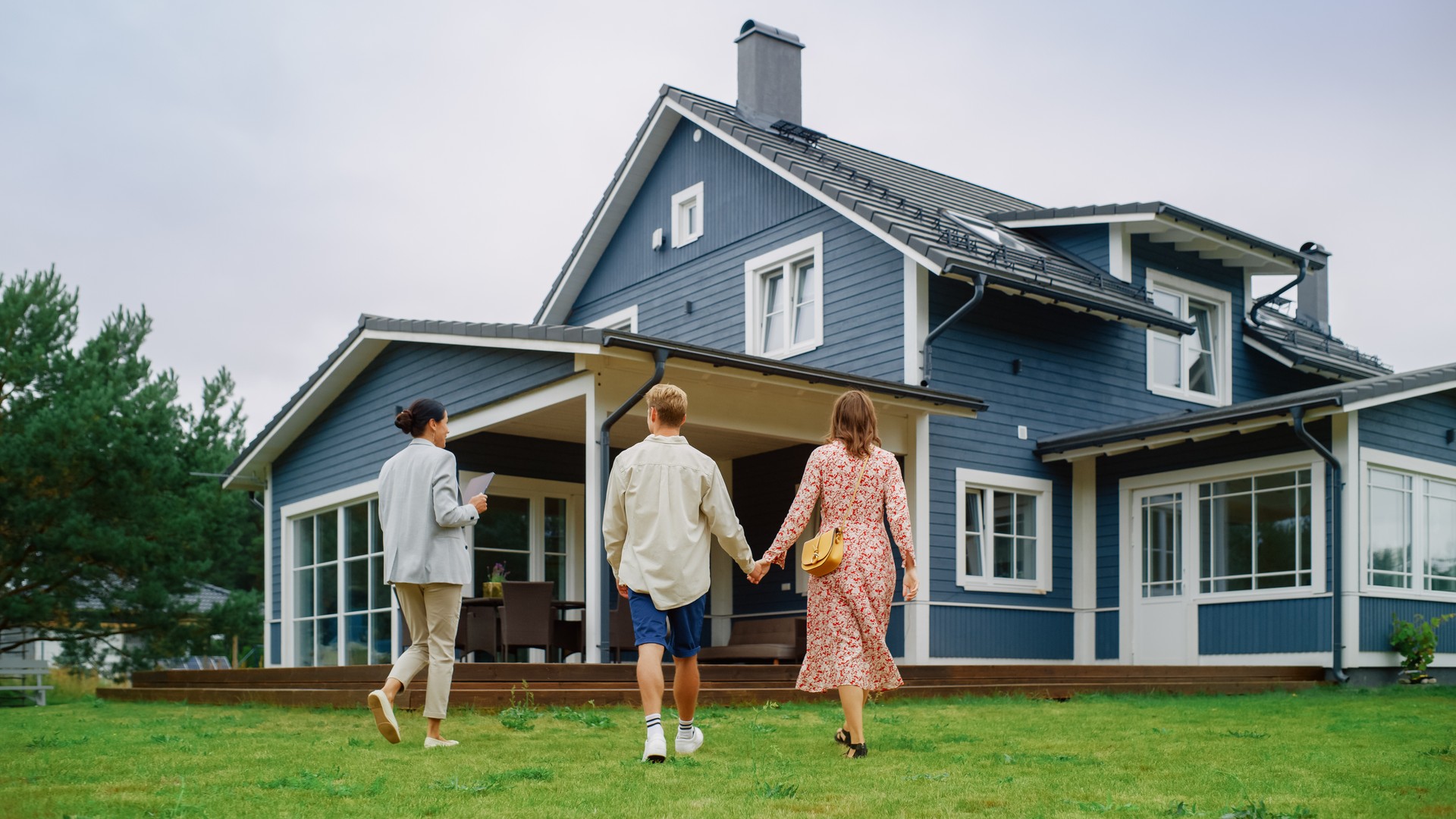 Young Couple Viewing Property for Sale, Talking with Professional Real Estate Agent Outside the House on a Summer Day. Young Beautiful Family are Ready to Become New Homeowners.